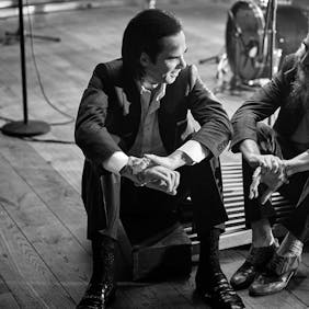 Nick Cave and Warren Ellis sitting on the floor in their Studio.